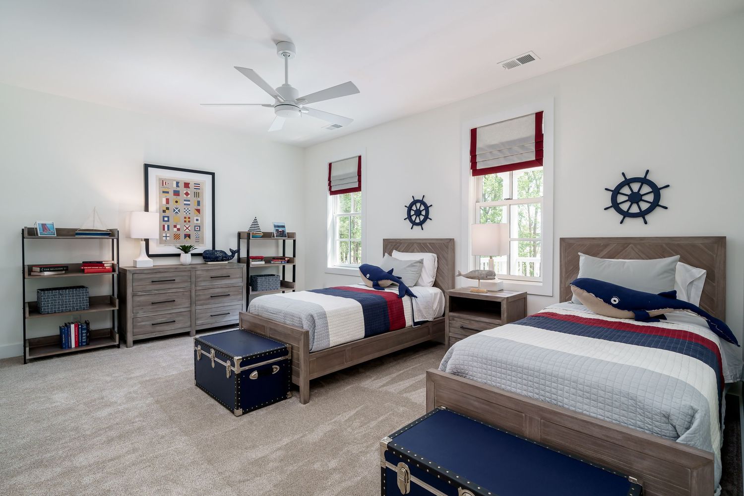 Model home nautical-themed bedroom featuring twin beds with navy accents, wooden furniture, and ship wheel wall decorations.