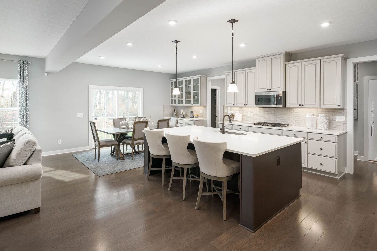 Model home builder open concept kitchen with white cabinets, dark wood island, and gray upholstered barstools in luxury home interior.