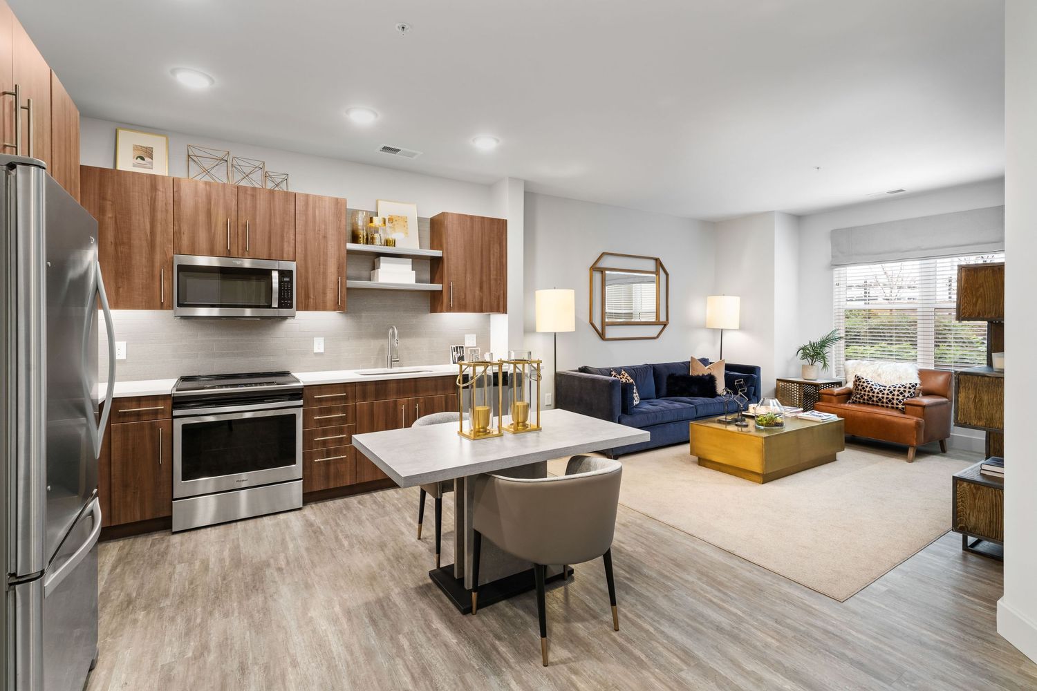 Modern open-concept apartment interior with stainless steel kitchen appliances and warm wood cabinetry flowing into living area.