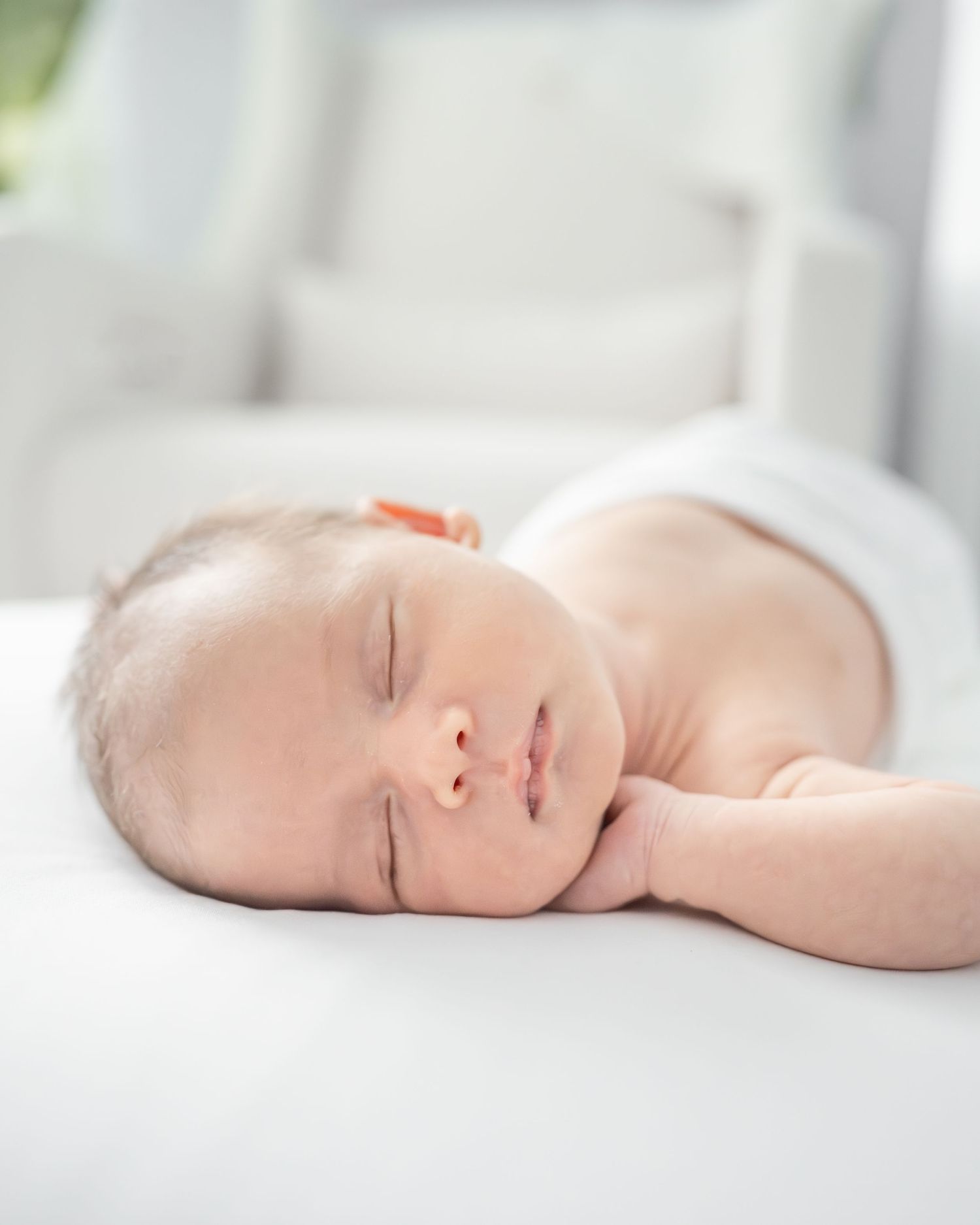 baby boy sleeping on white bean bag in nursery, with his hand tucked up under his cheek