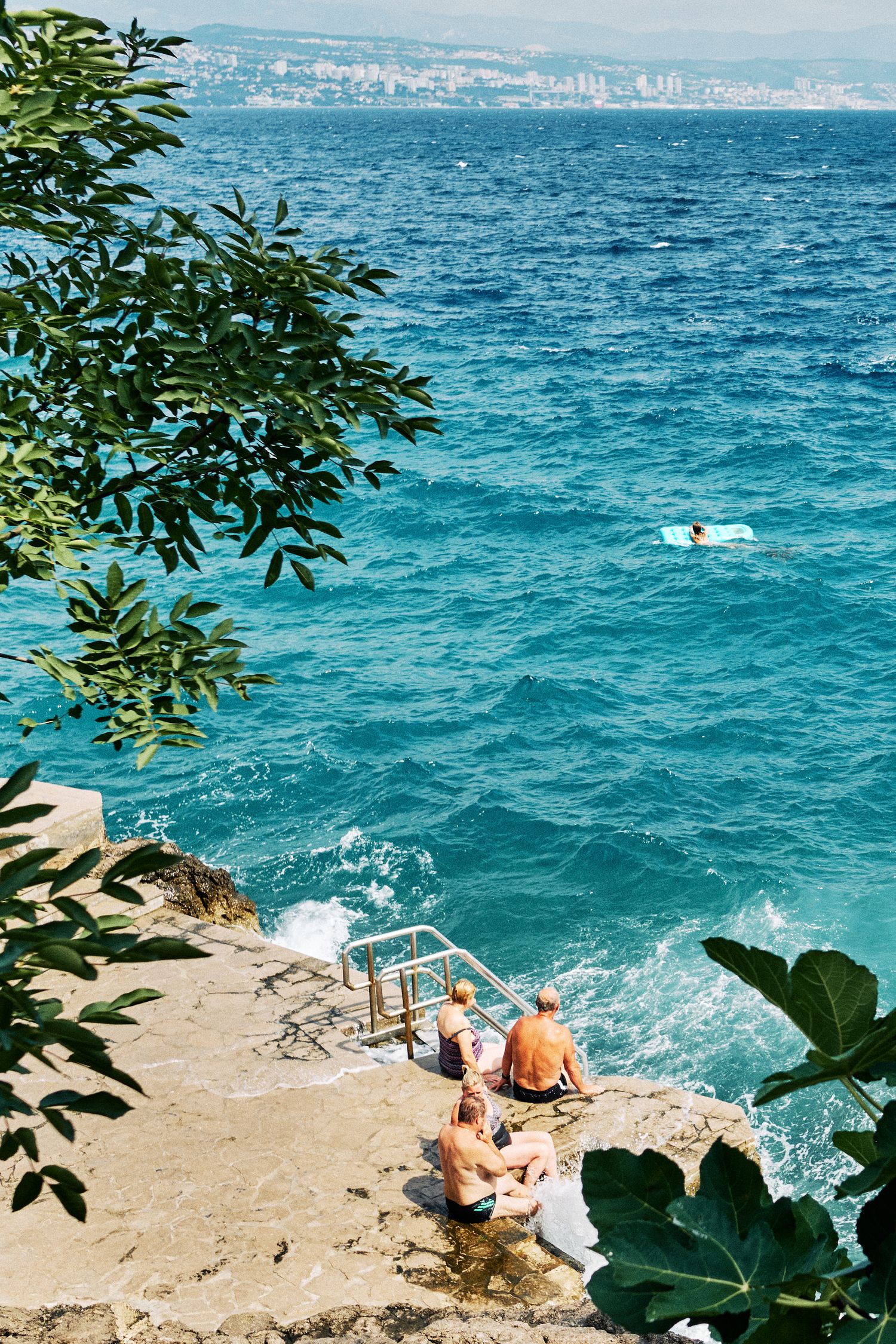 People relaxing on rocky outcrop overlooking blue ocean waves.