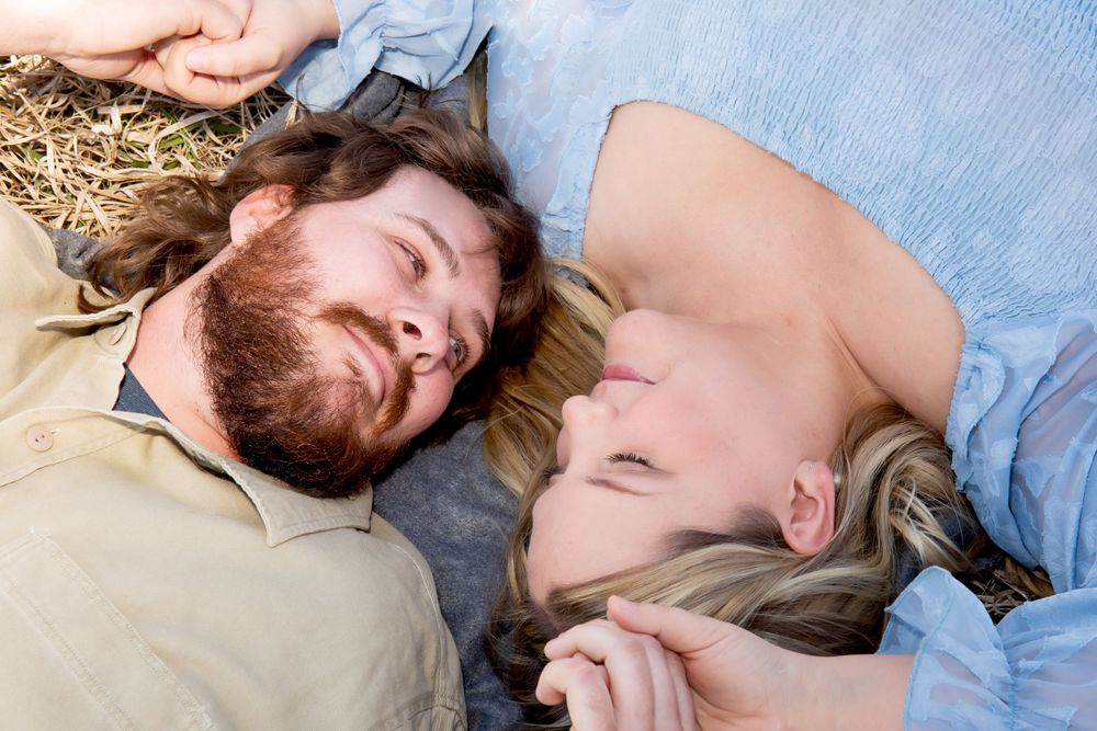 A couple lying on dry grass smiling together in romantic outdoor photo shoot.