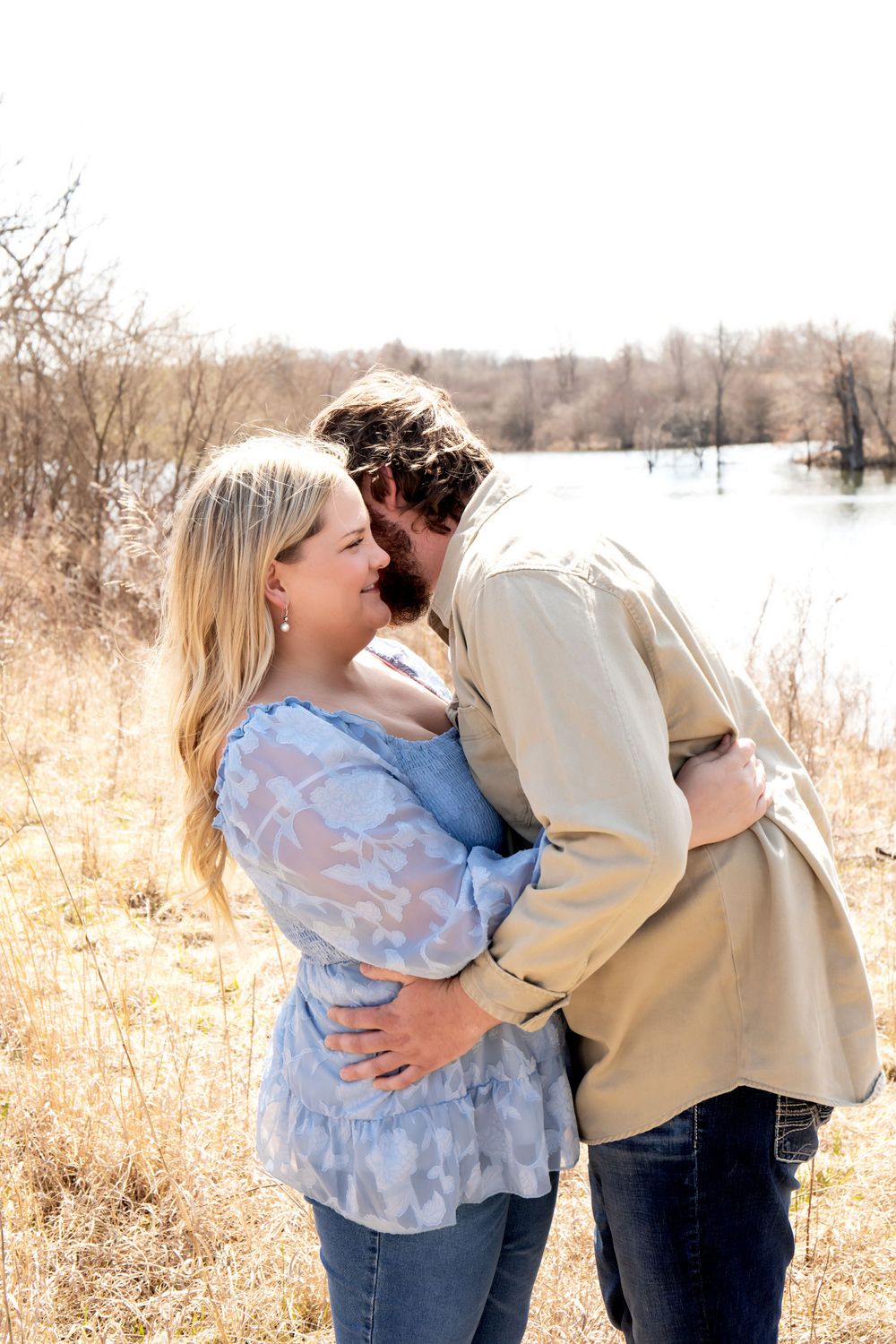 A romantic couple shares an intimate moment by a lake during a golden hour photoshoot.