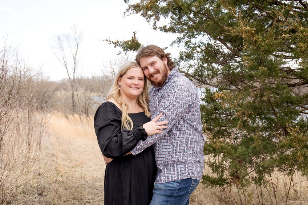 Couple poses together near an evergreen tree during an autumn engagement shoot.