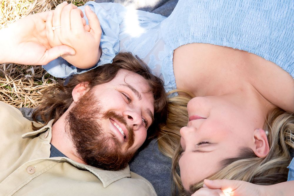 Couple laying head to head on hay in casual outdoor photo session.