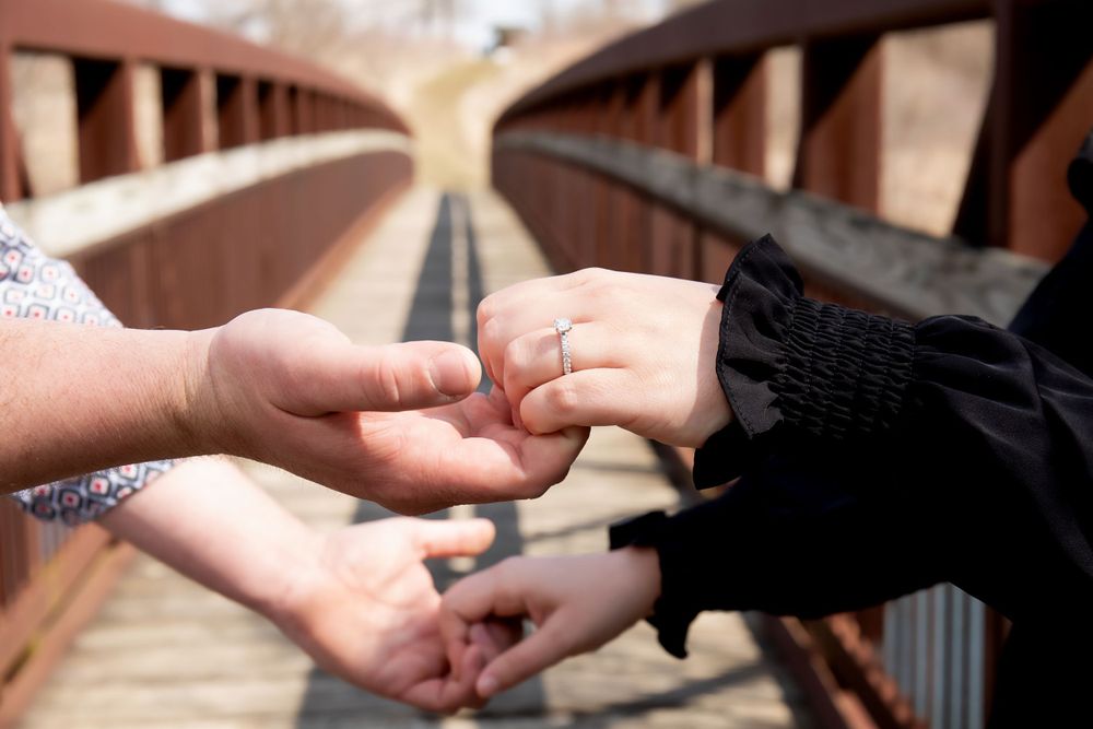 Close-up shot of hands exchanging rings during an outdoor bridge proposal.