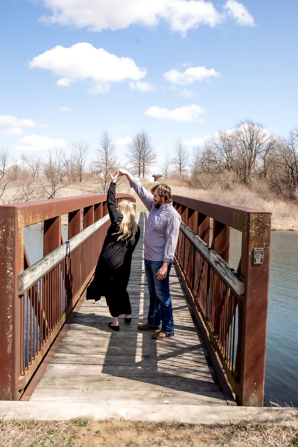 Two people dancing and laughing together on a wooden bridge with blue sky overhead.