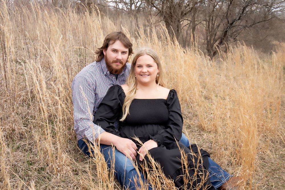 Couple sitting together in tall autumn grass during a countryside photoshoot.