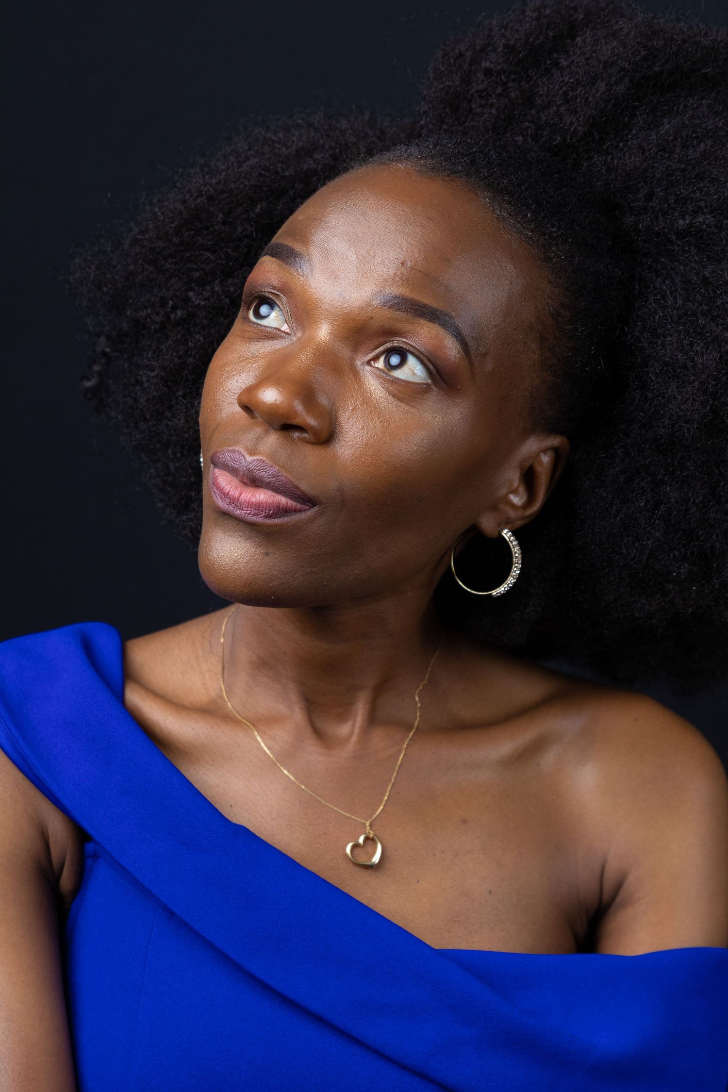 Portrait of woman in blue asymmetrical top with natural hair against dark background.