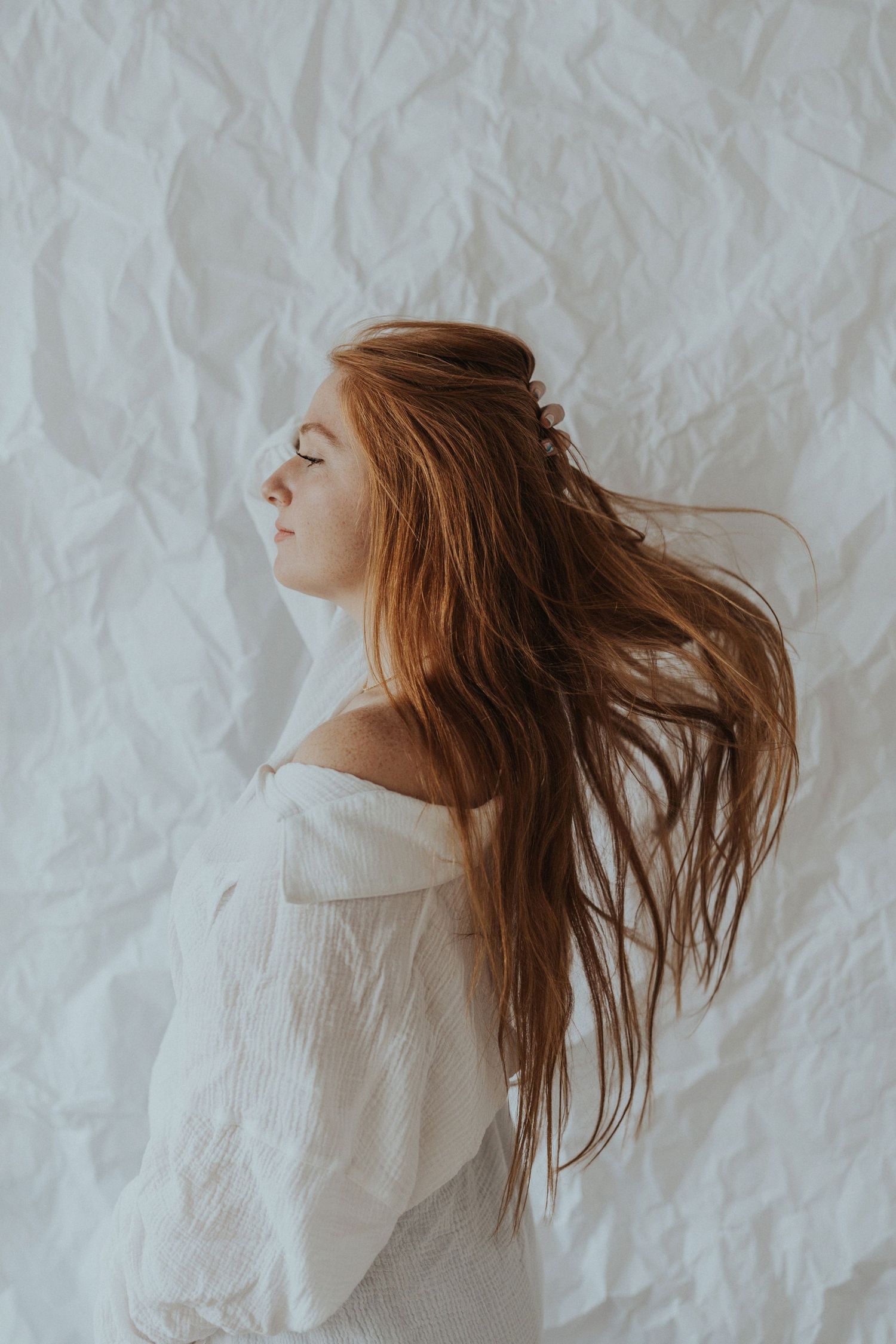 A redhead girl stands against a white paper backdrop