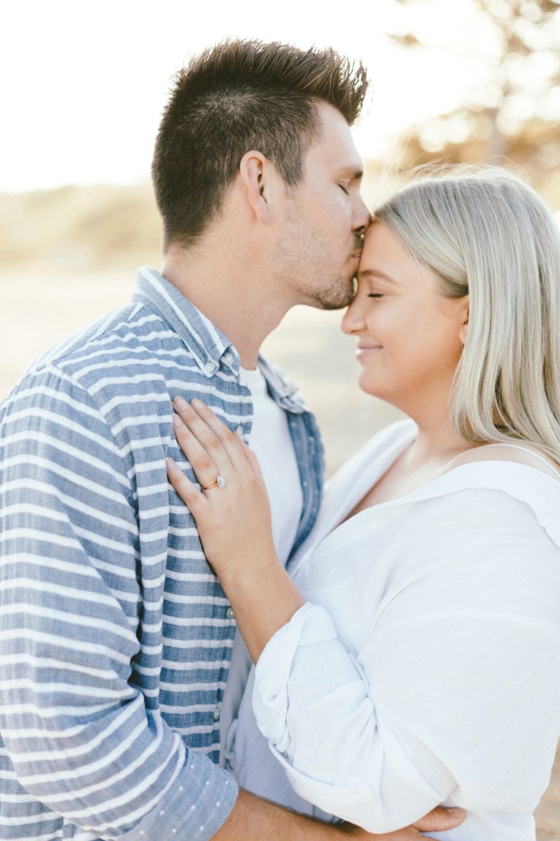 A tender moment shared between a couple in casual striped and white attire showing an engagement ring.