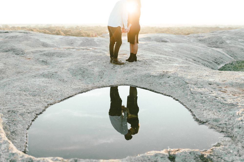 Couple walking along a rocky coastal area during sunset, casting long shadows on the ground.