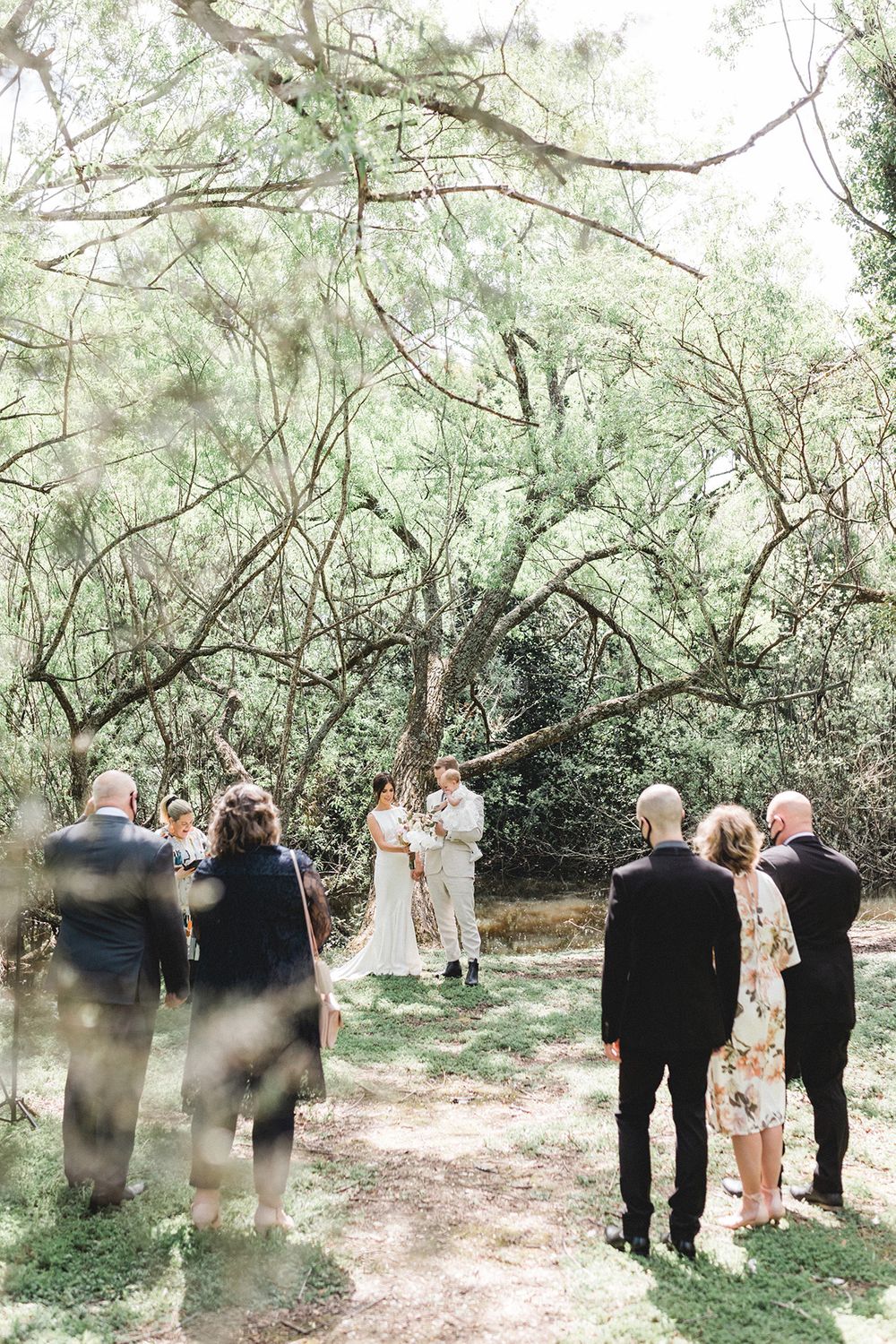 Intimate outdoor wedding ceremony under a canopy of green trees.