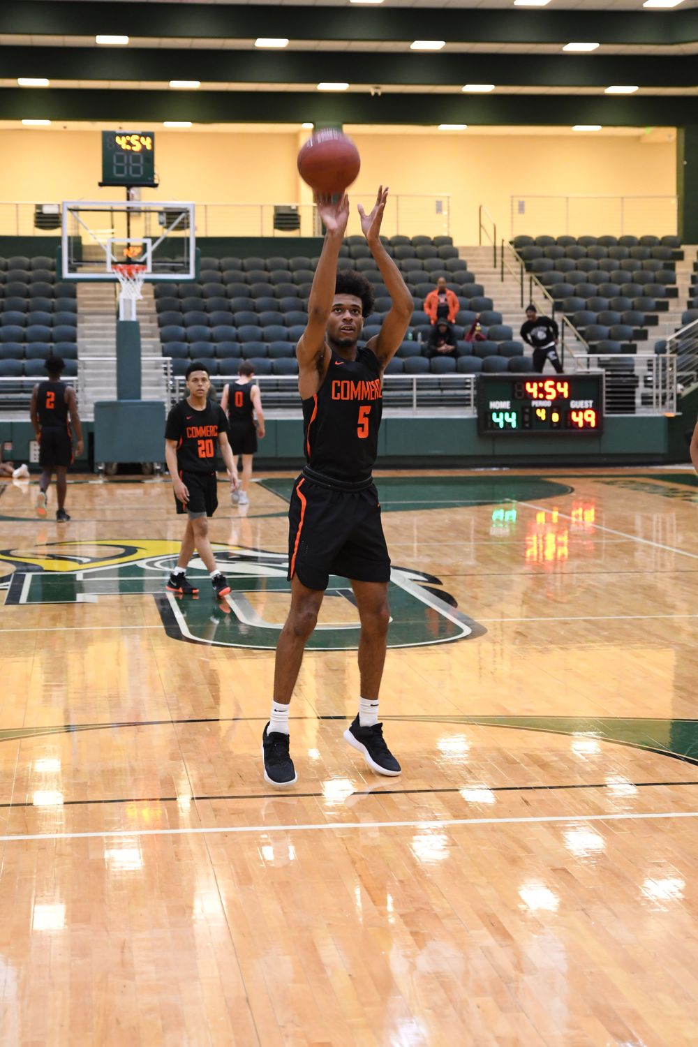 Basketball player in black uniform takes jump shot on indoor court.