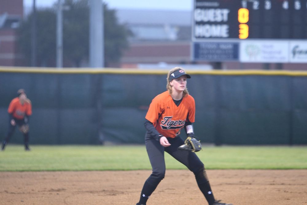 Infielder in orange jersey ready in defensive stance during baseball game.