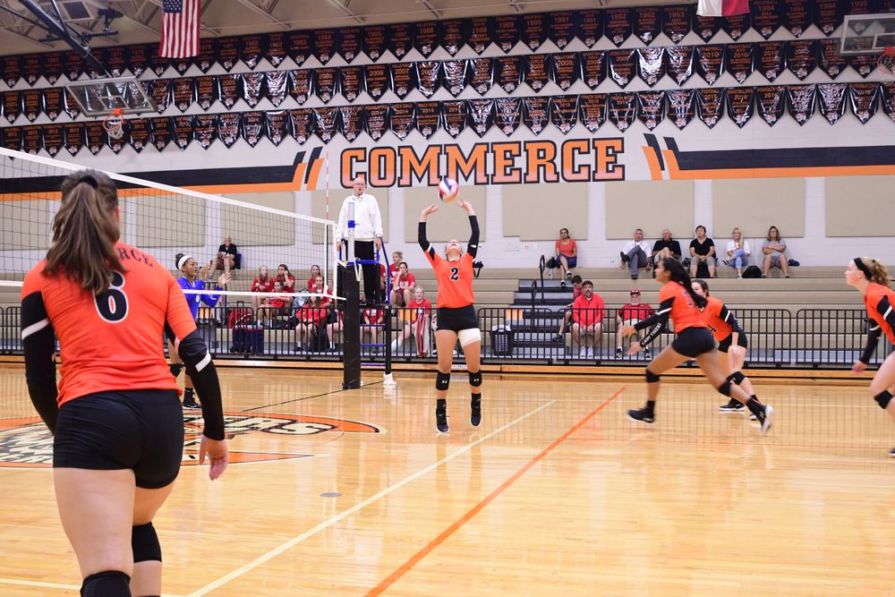 Volleyball players compete at the net in school gymnasium during match.