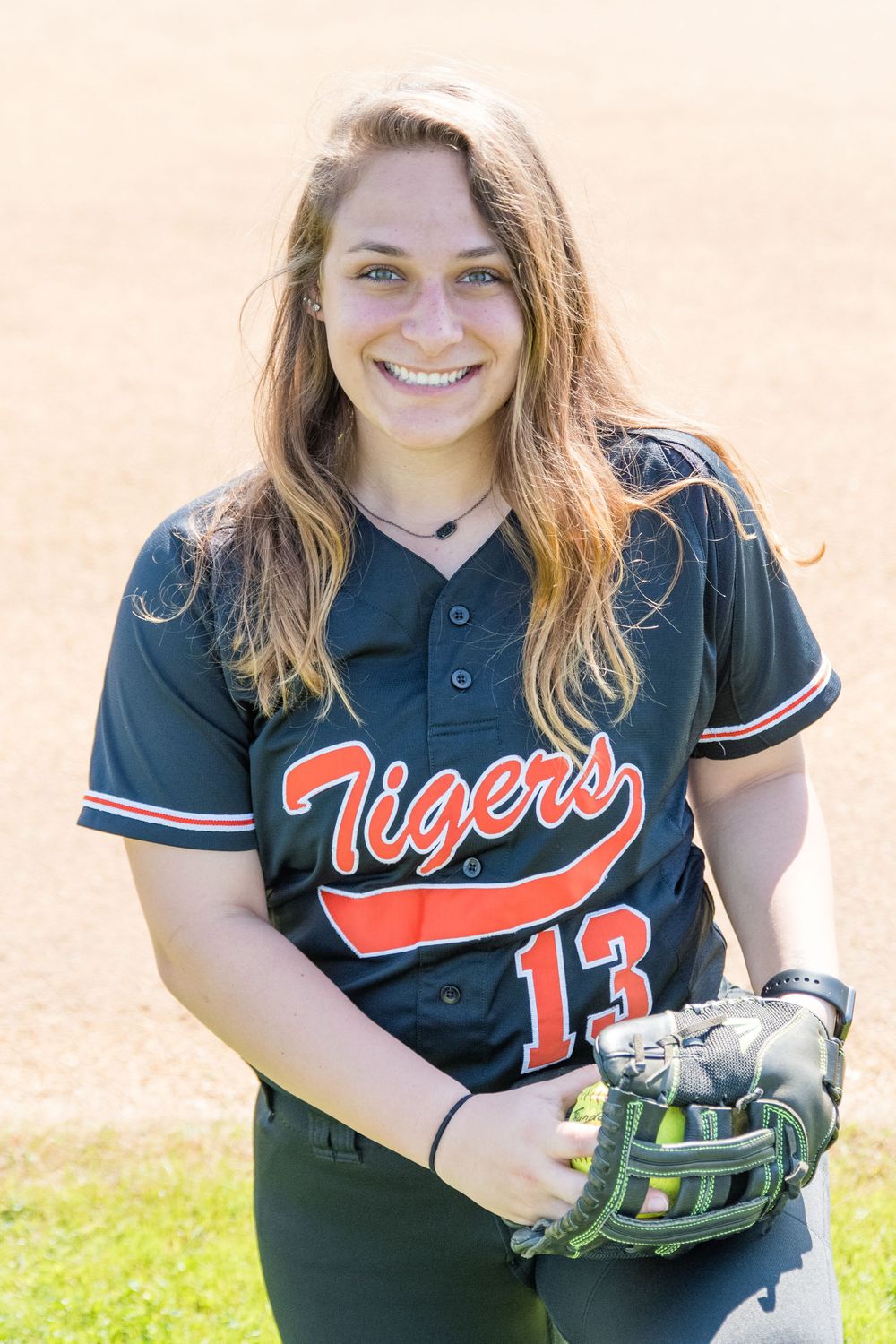 Softball player wearing navy Tigers jersey number 13 with glove on field.