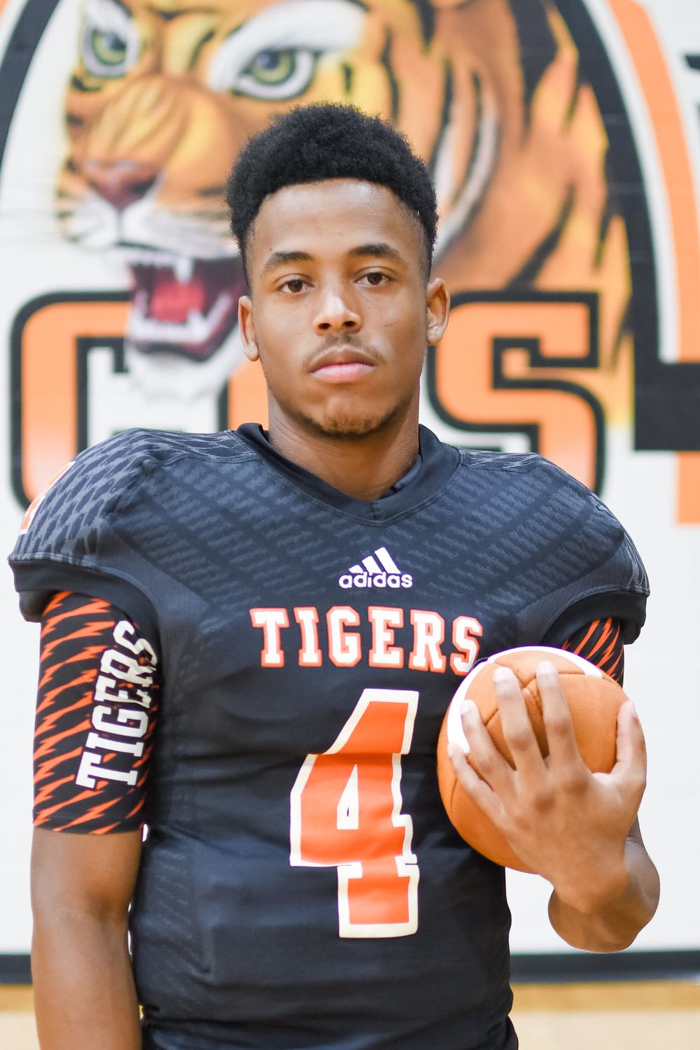 Football player in black Tigers jersey number 4 standing in front of team mascot logo.
