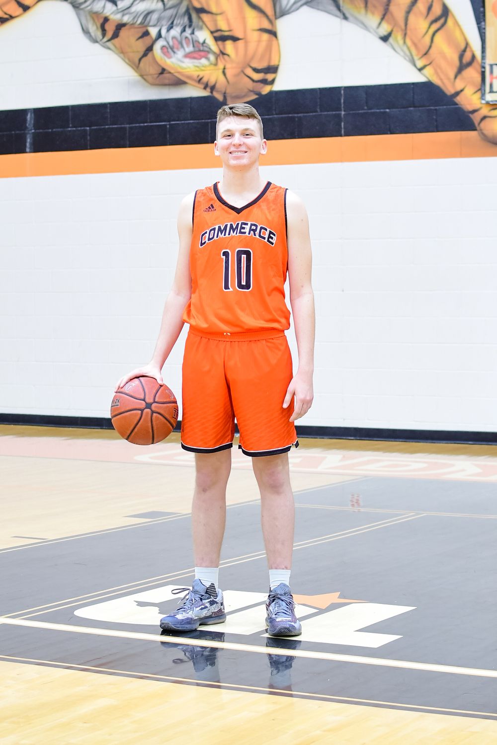 Basketball player in orange uniform holding ball on indoor court with tiger mascot mural.
