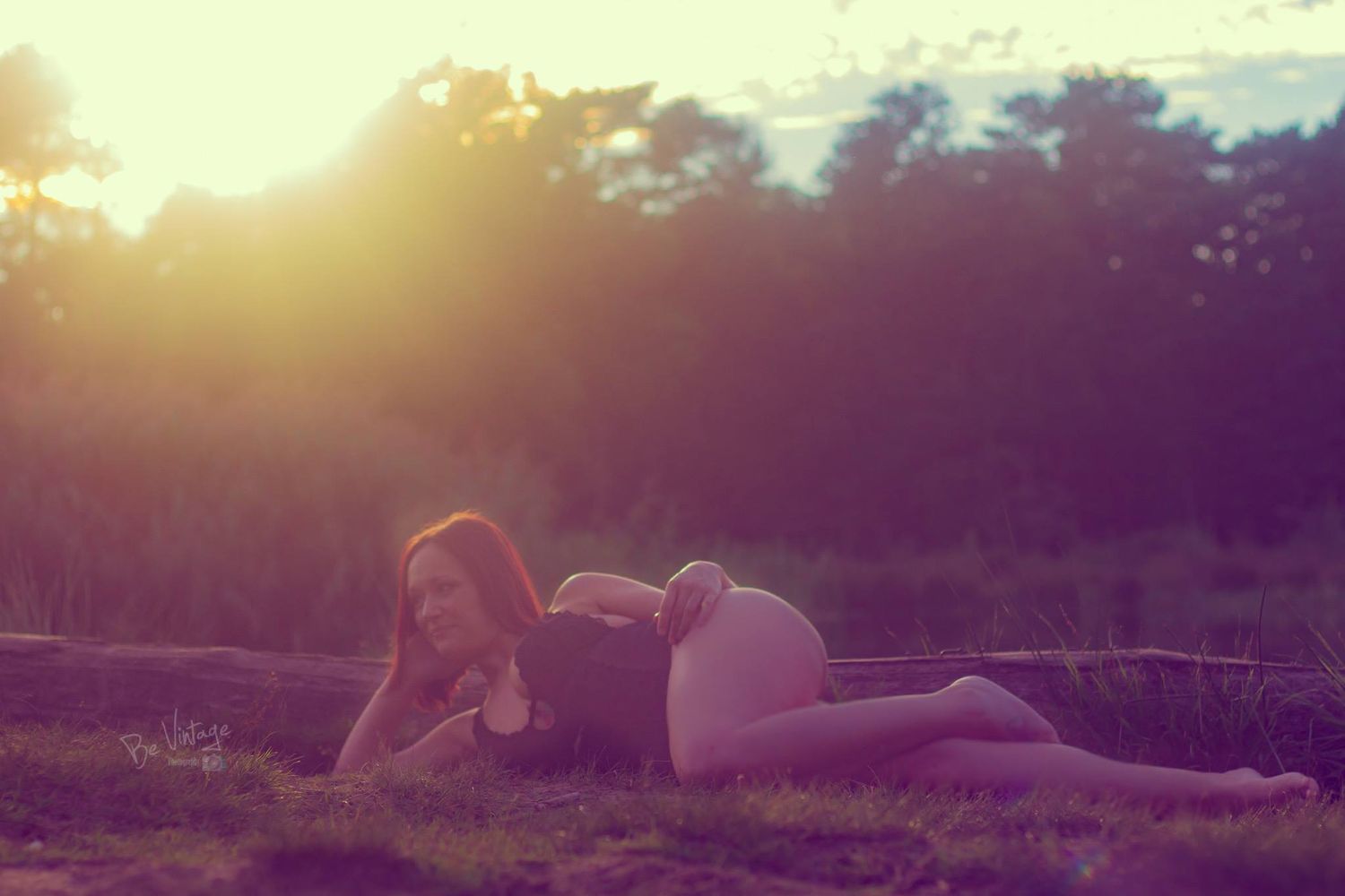 Woman lying in a field at sunset with warm golden light and lens flare creating a dreamy atmosphere.