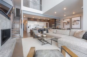 A modern, open-concept living space with high ceilings and neutral tones. The room features a large, sectional sofa.