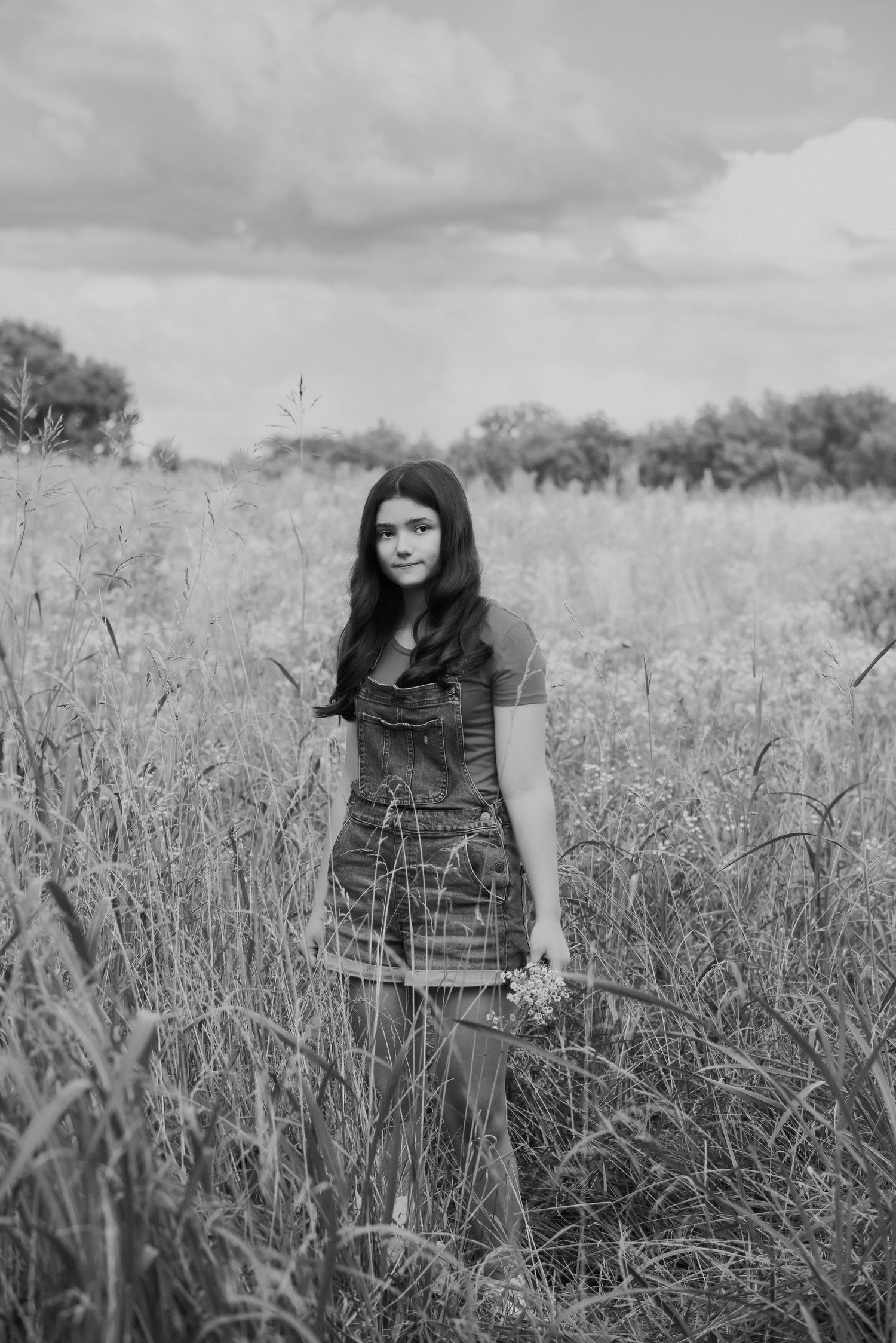 girl stands holding wildflowers in grassy field