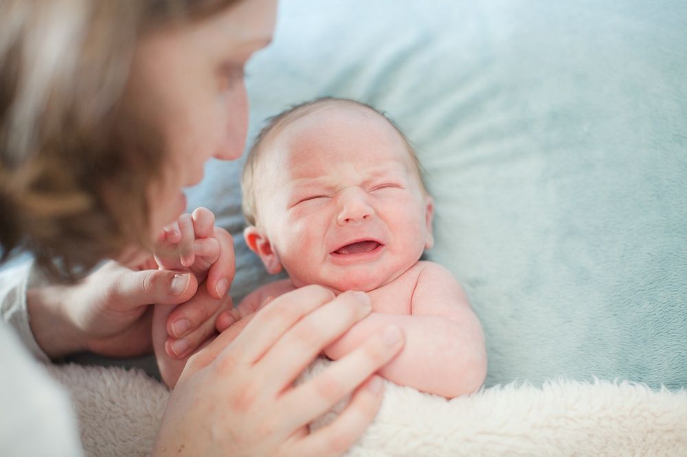 Gentle moment of newborn baby being cradled on soft blue blanket.