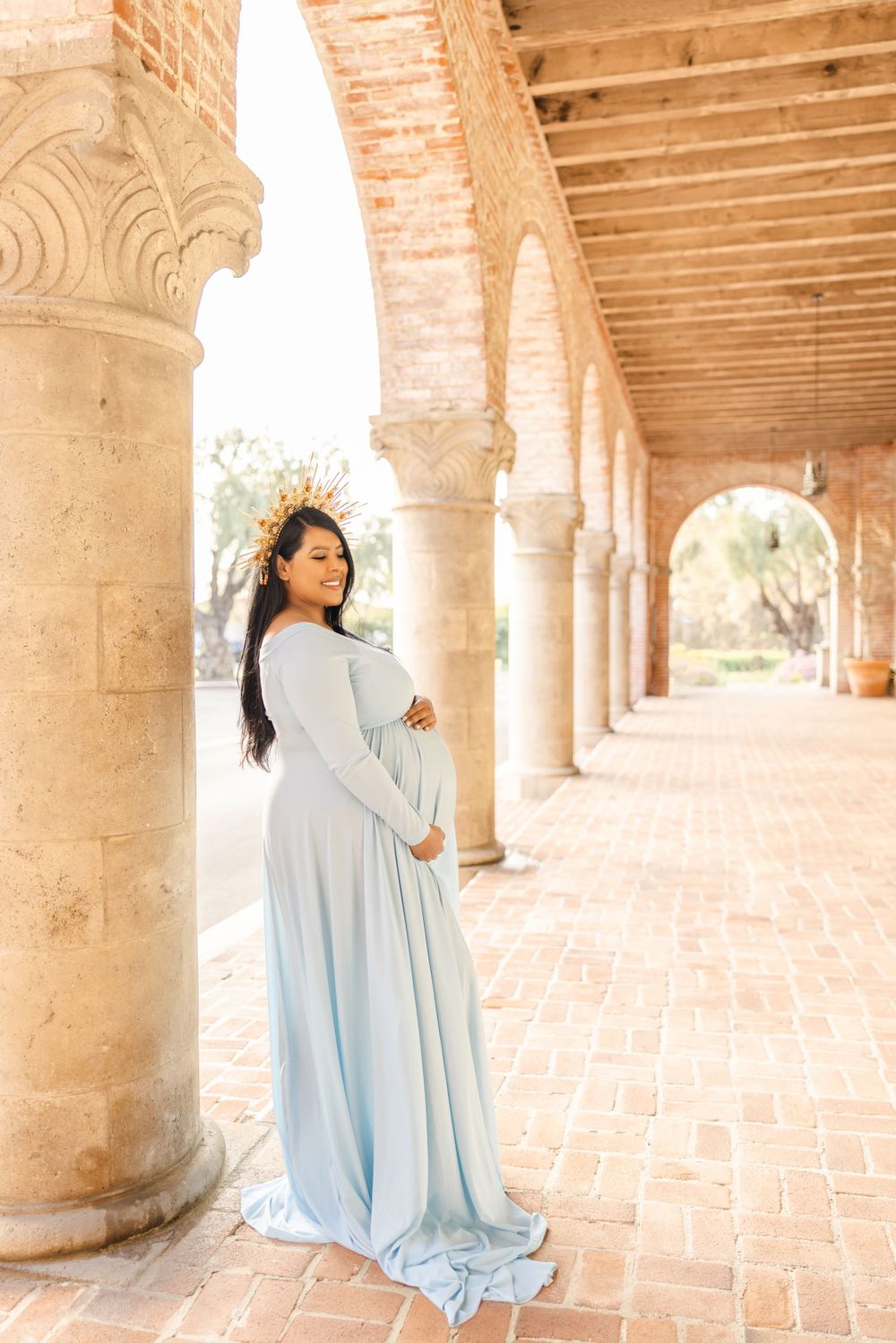 A woman in an ethereal blue gown stands among ornate stone columns in warm sunlight.