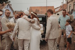 Wedding celebration in front of a vintage car with guests dressed in beige and white tones.