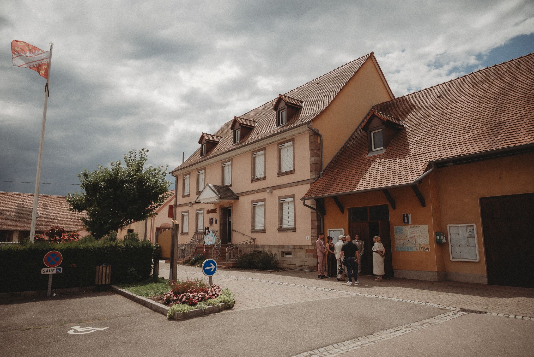 Traditional European village buildings with orange and brown facades under cloudy skies.