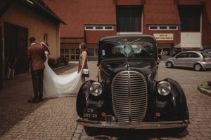 Classic vintage black car parked on cobblestones with wedding party and flowing white dress.