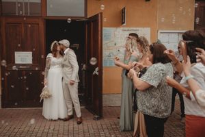 Wedding guests blow bubbles as the newlywed couple celebrates outside a building entrance.