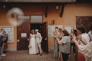 Wedding guests celebrate and blow bubbles while the couple poses in front of wooden doors.