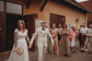 Wedding party in cream and neutral tones walks together outside a building with terracotta walls.