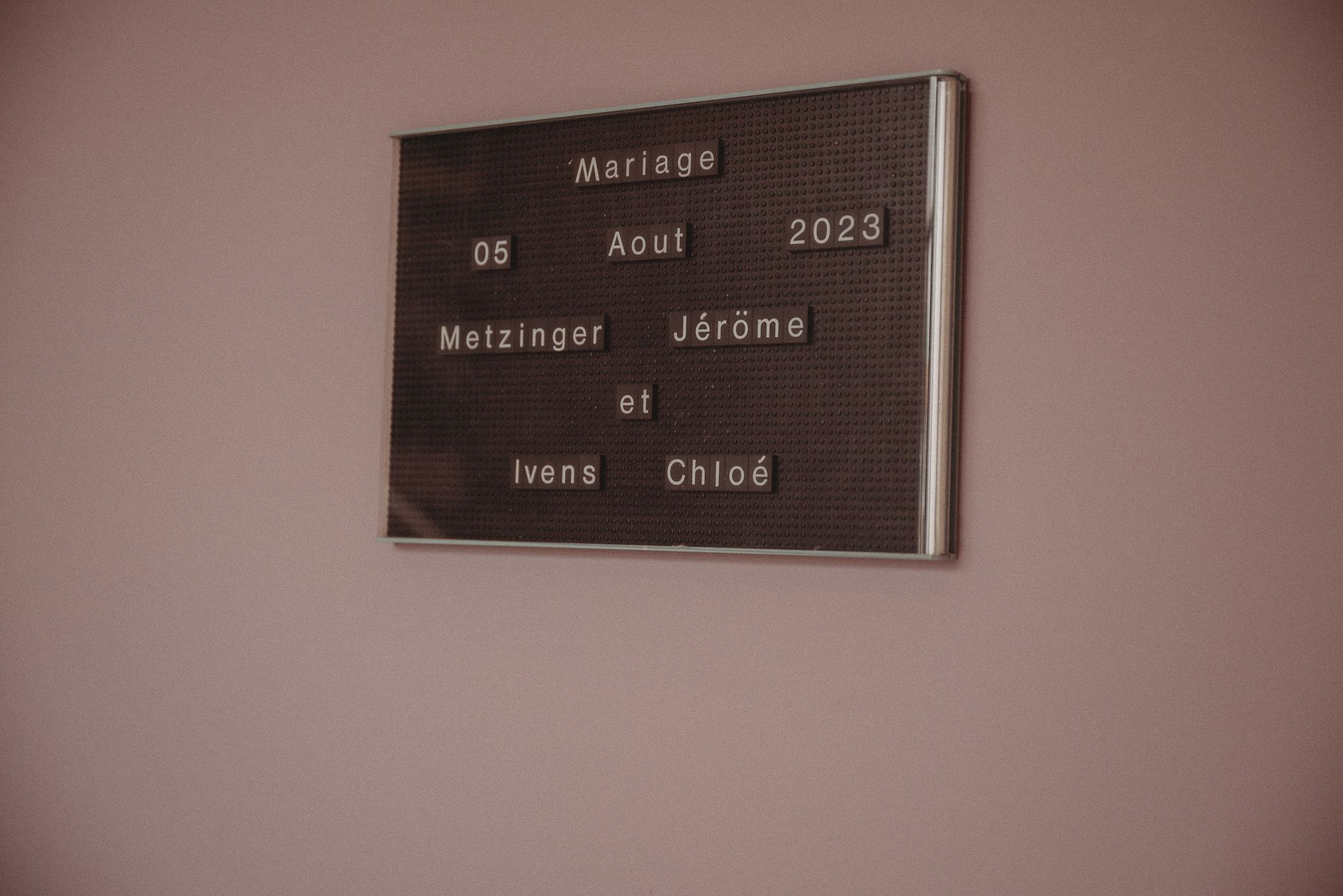 Wedding date and names displayed on dark memorial plaque mounted on pink wall.
