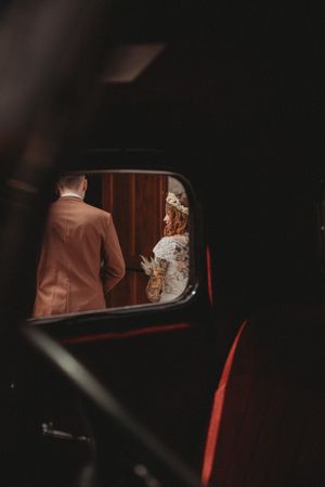 Artistic reflection in vintage car mirror shows couple in wedding attire.