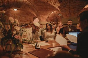 Wedding couple signing documents at a wooden table in a brick-vaulted cellar.