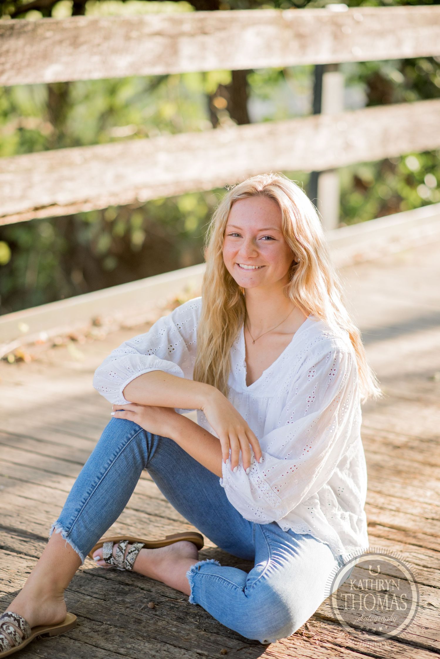 A relaxed outdoor portrait featuring a white eyelet blouse and jeans on a wooden bridge in natural lighting.