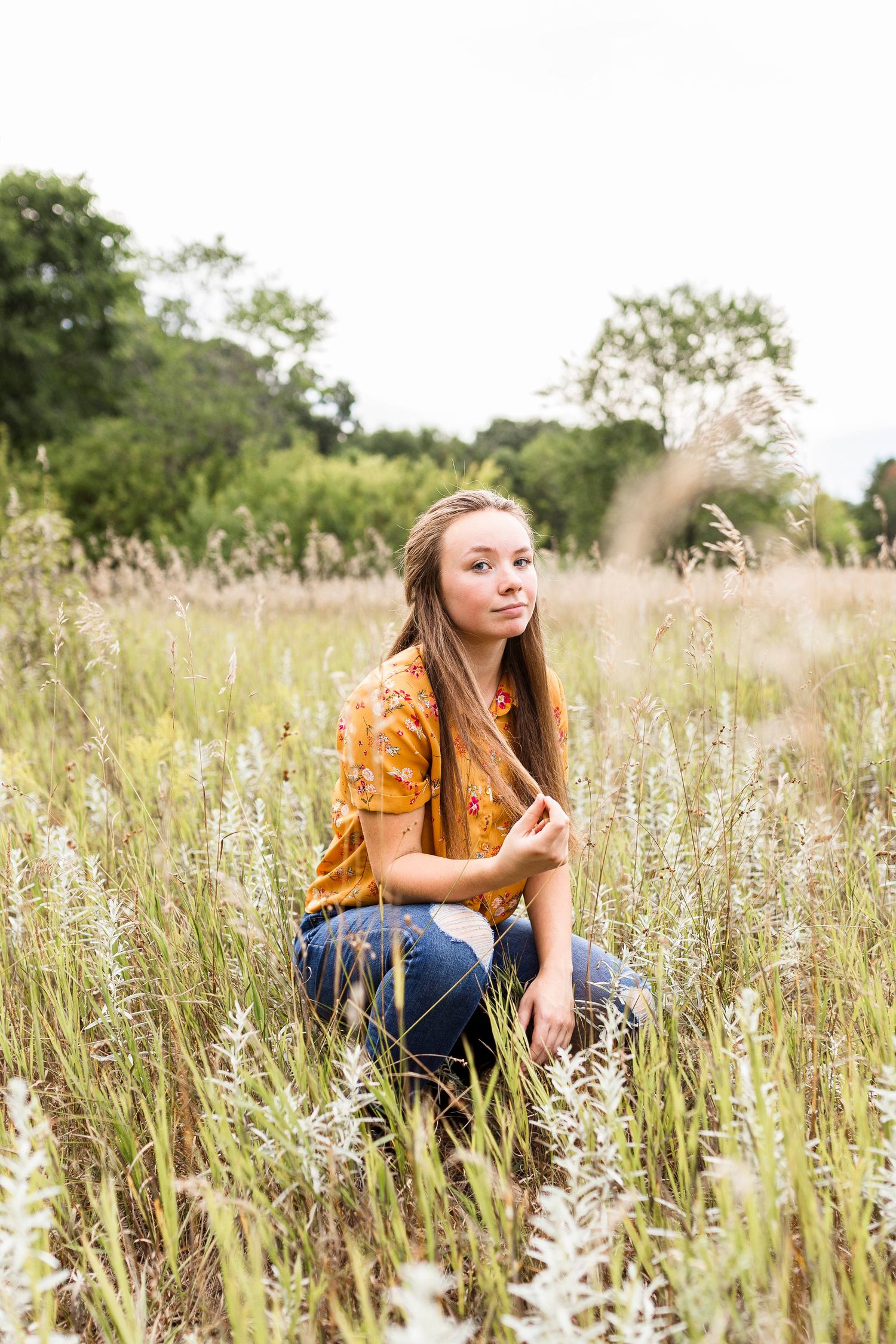 A woman in orange sits among tall wildflowers in a summer meadow.