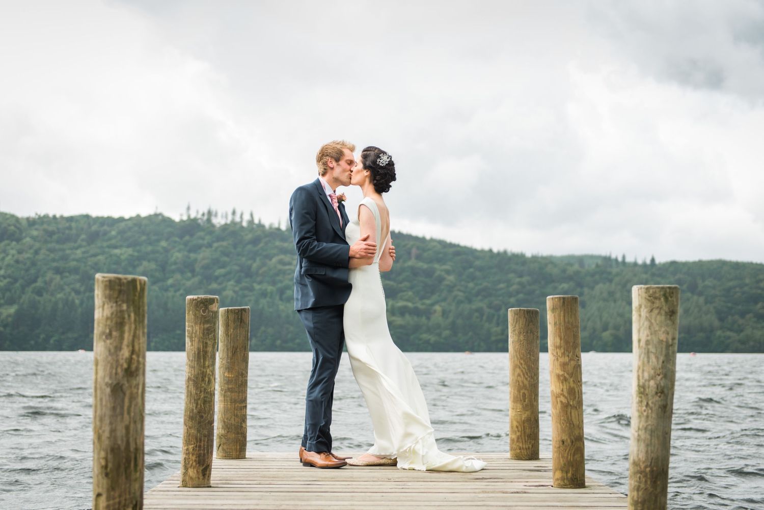 Couple in wedding attire kissing at the end of a jetty on Lake Windermere