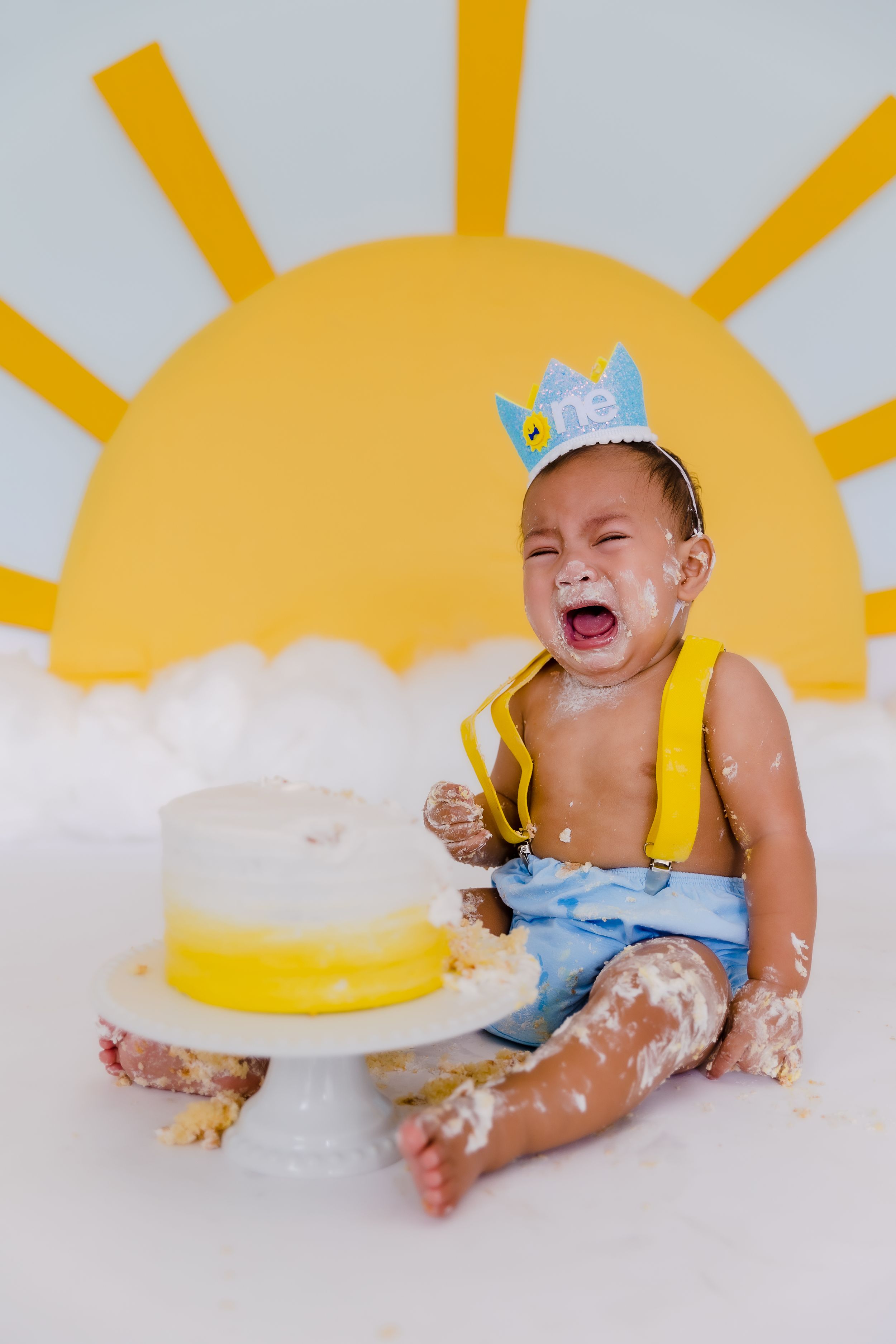 Baby in yellow outfit having fun with cake smash photo session.