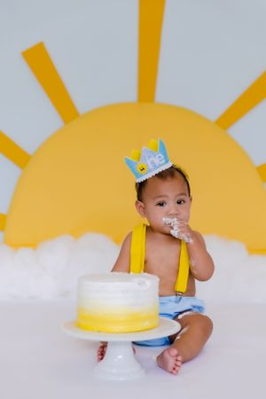 Baby in blue outfit reaching for cake during first birthday photoshoot.