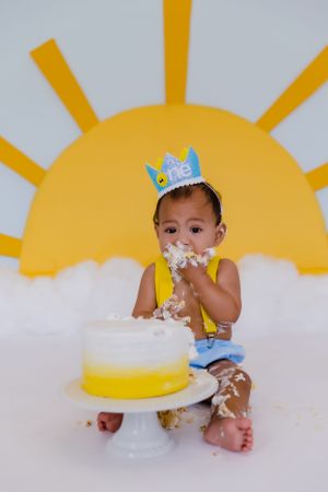 Baby enjoying messy cake smash session with yellow sun wall decoration.