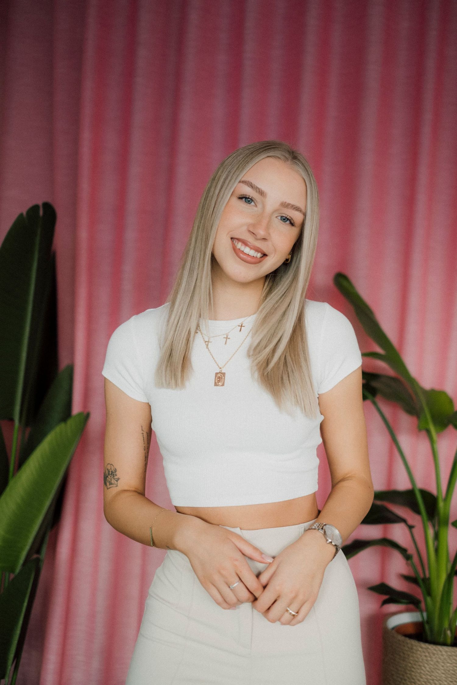 Lifestyle portrait with pink curtain backdrop and tropical plants.