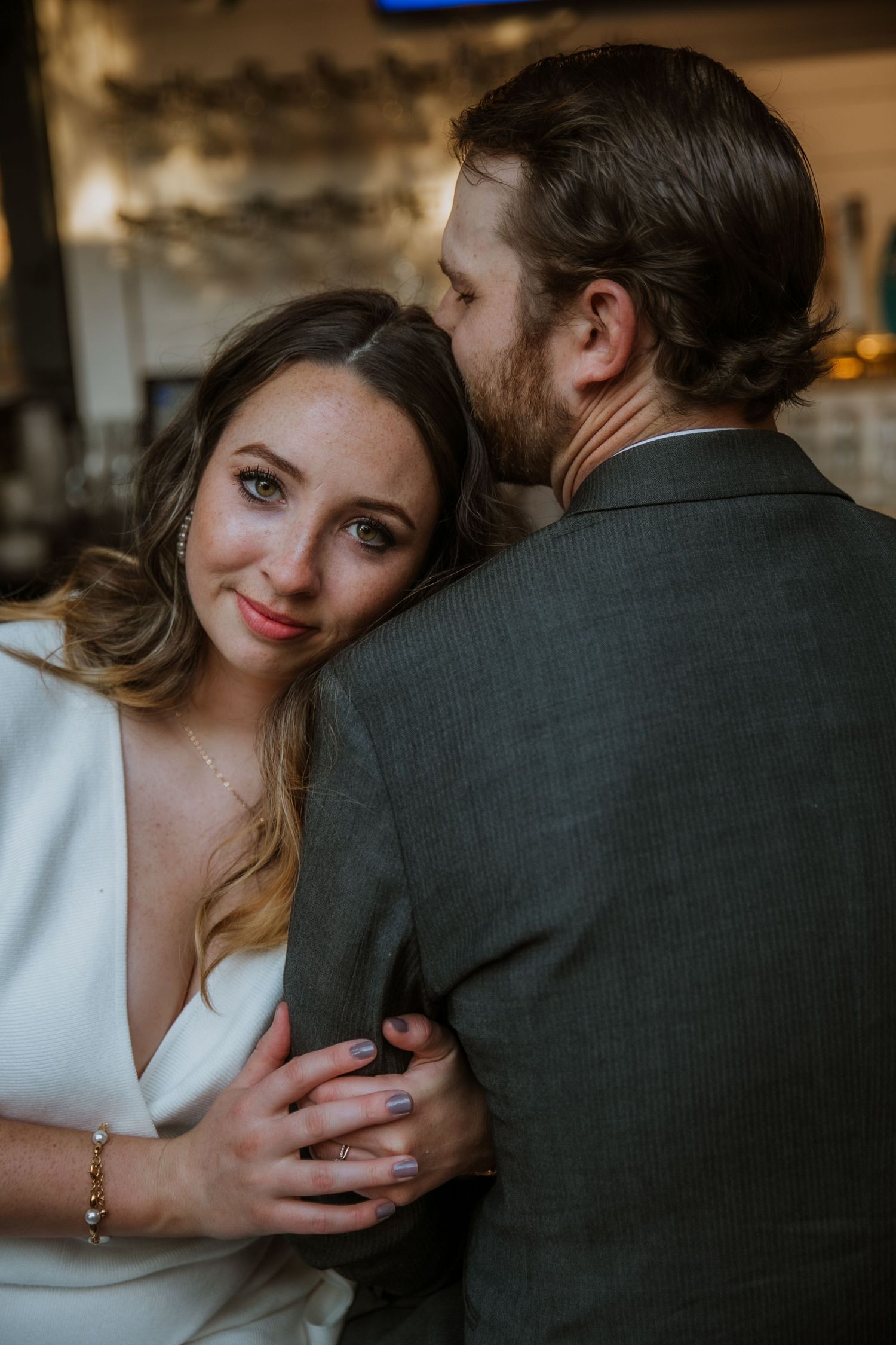 A man kisses a woman on her head while she looks at the camera