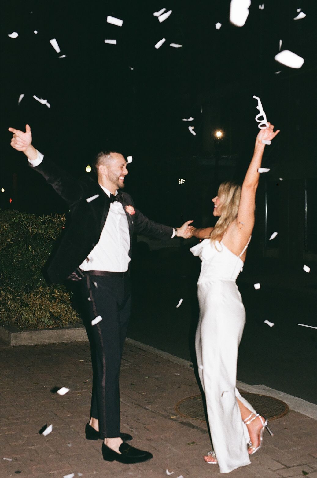 Couple celebrates joyfully with confetti falling at a nighttime wedding celebration.