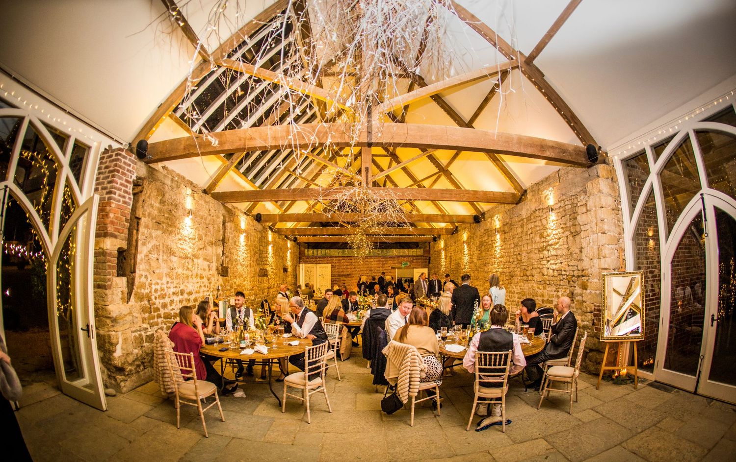 Panoramic view of a rustic barn wedding venue with exposed wooden beams and ambient lighting.