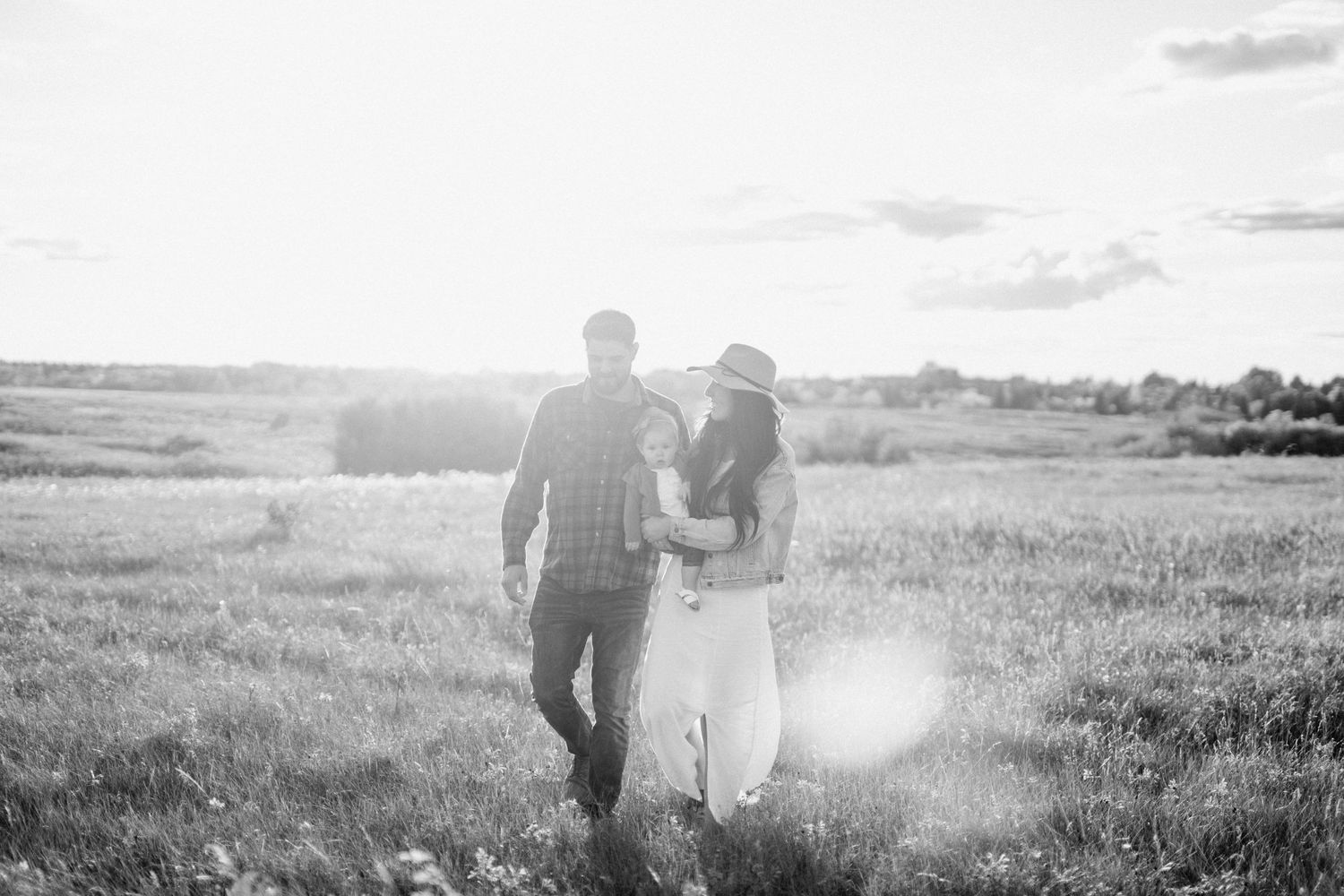 Romantic black and white portrait of couple walking through sunlit field.