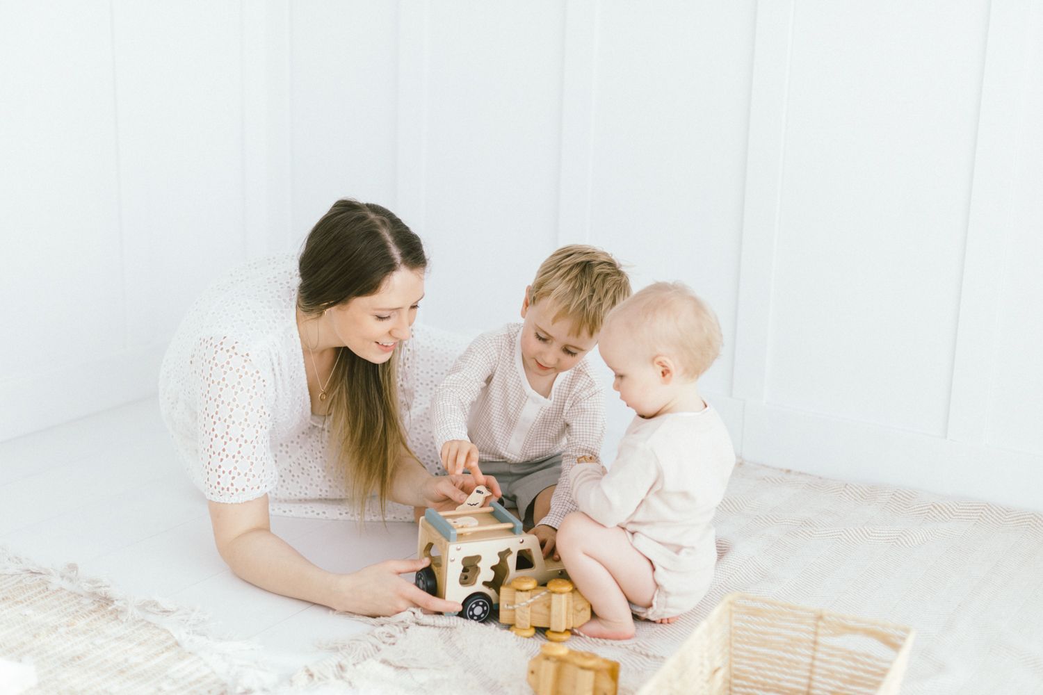 Family plays with wooden toys on white floor in minimalist setting.
