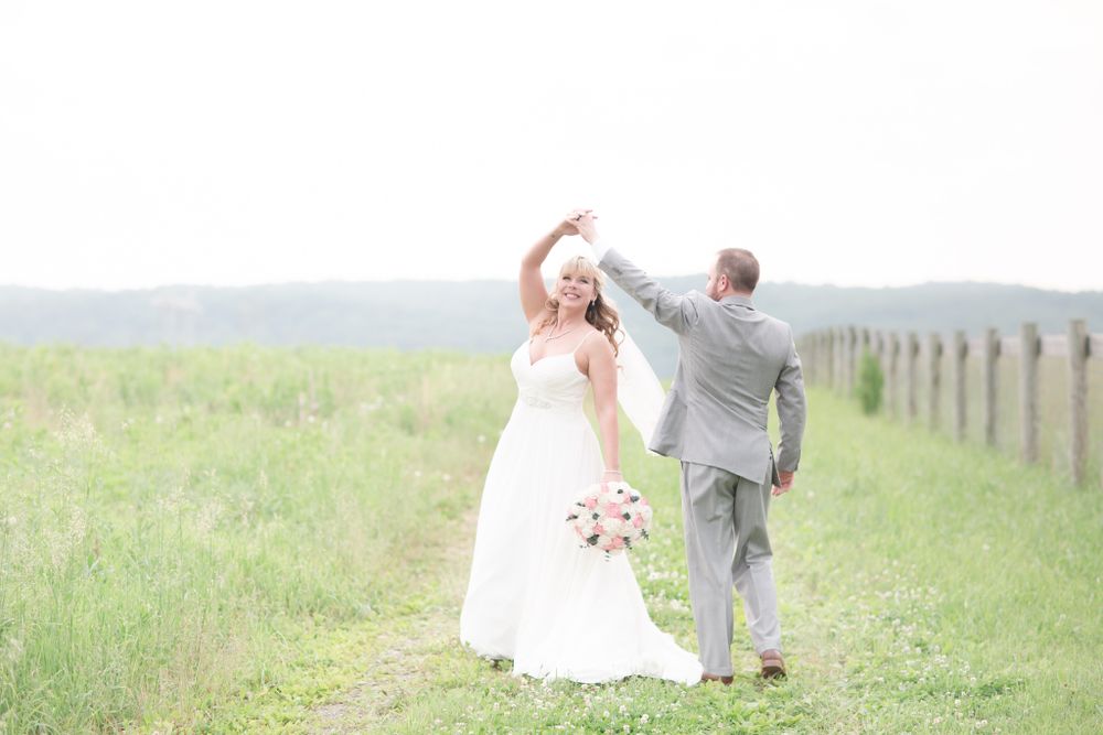 A couple celebrates joyfully while walking through a scenic countryside field on their wedding day.
